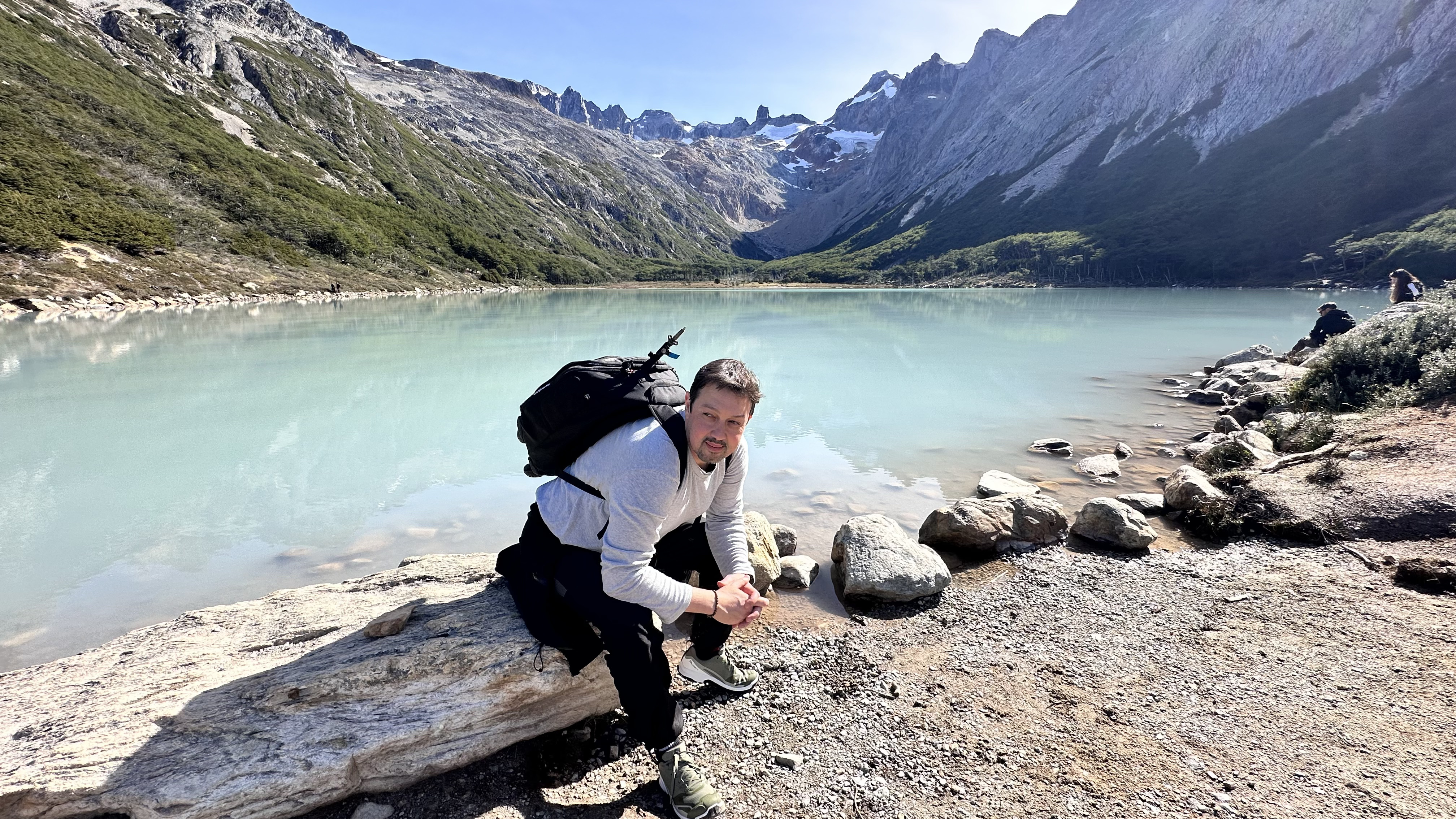 Jeff Gonzalez sentado na margem da Laguna Esmeralda em Ushuaia, água turquesa e montanhas ao fundo