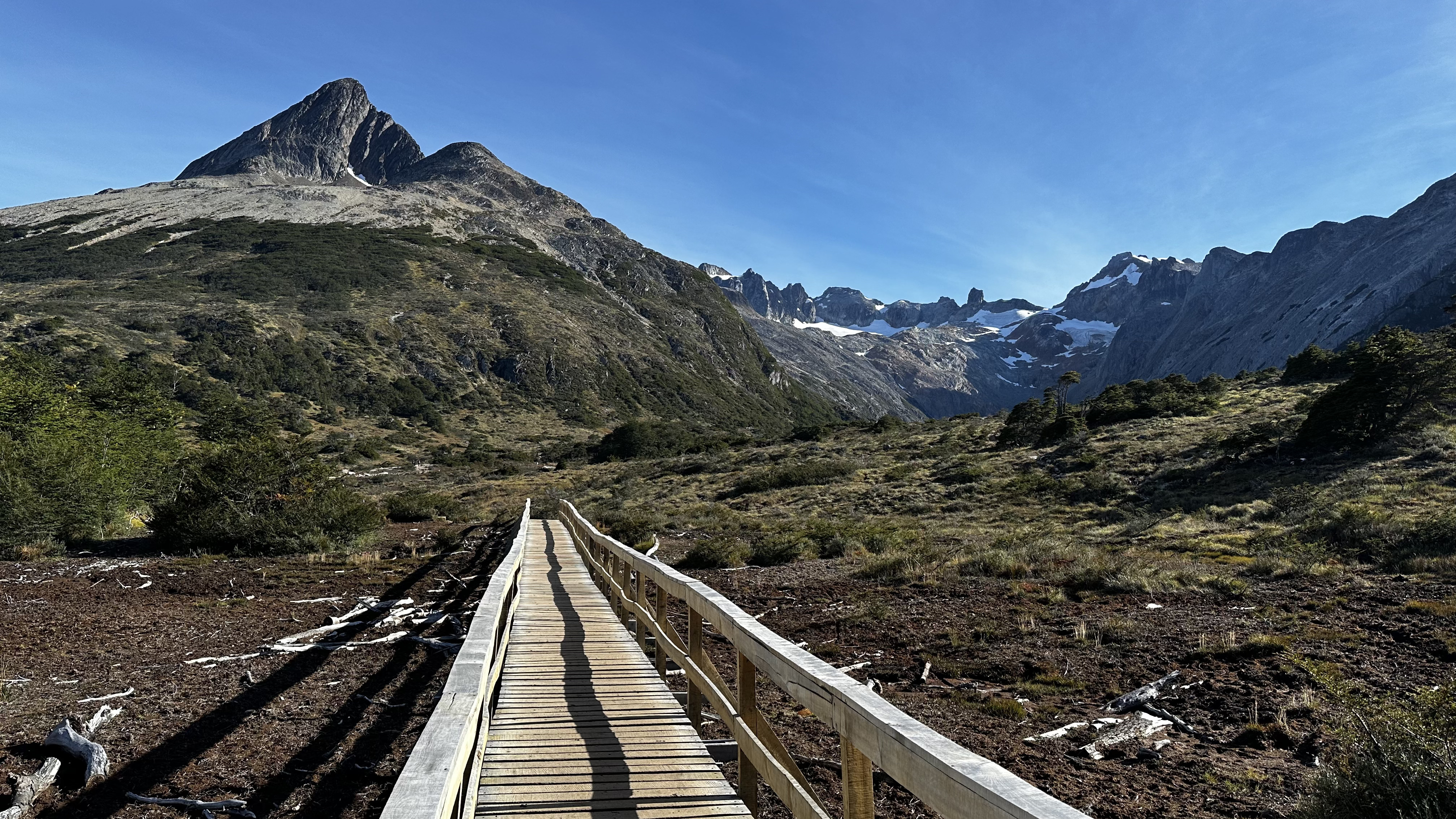 Passarela de madeira sobre o turbal na trilha da Laguna Esmeralda, com montanhas nevadas ao fundo